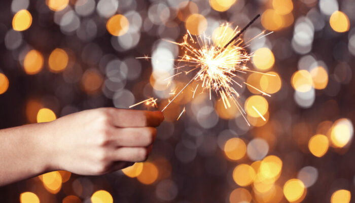 Female hand holding sparkler against colorful defocused lights